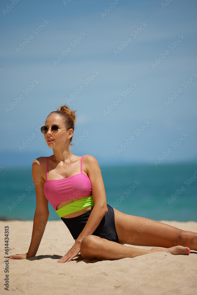Young woman sitting on sandy beach in colorful swimsuit at Seychelles, summer vacation concept