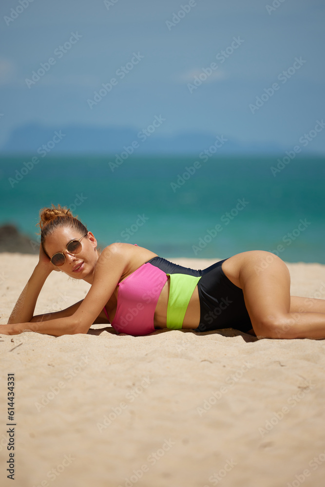 Beautiful young woman in bikini lying on the sand of tropical beach