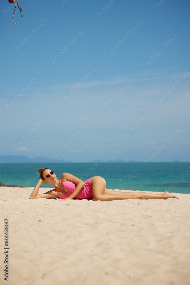 Beautiful young woman the sun in pink swimsuit sunbathing on the beach, she lays down on sandy beach under the sun. Travel vacation concept