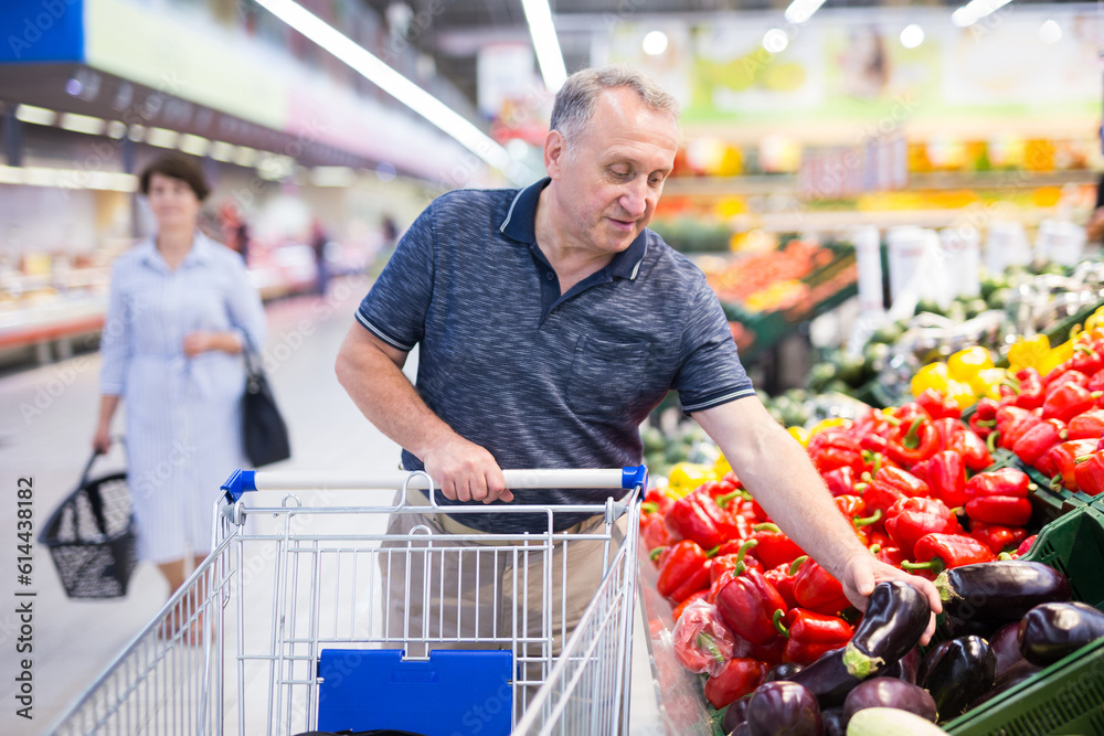 elderly retired man buying eggplants in grocery section of the supermarket