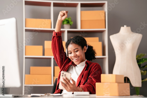 Small business parcel delivery concept, African entrepreneur checking online order on laptop and raising arm to celebrate for successfully while working about delivery shopping online sales business