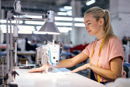 concentrated blonde caucasian woman seamstress sits using modern sewing machine. lady working in textile workshop. Tailoring  sewing as a small business or hobby concept. sewing process