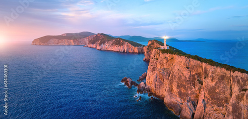 Panoramic, aerial view of Cape Ducato cliffs and sea with lighthouse shining, illuminated by pink light of setting sun. Lefkada, Greece.