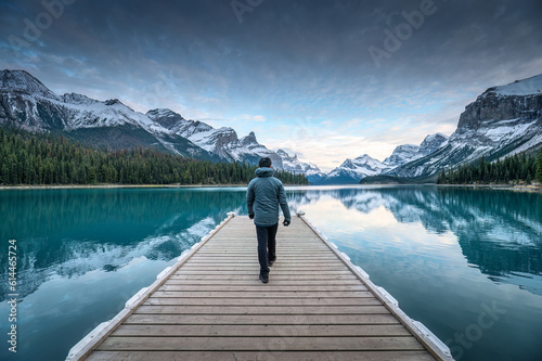 Male tourist walking on wooden pier among world famous iconic Spirit Island on Maligne Lake at Jasper national park