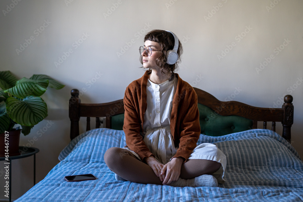 Relaxed teenage girl wearing headphones sitting on bed in lotus pose ...