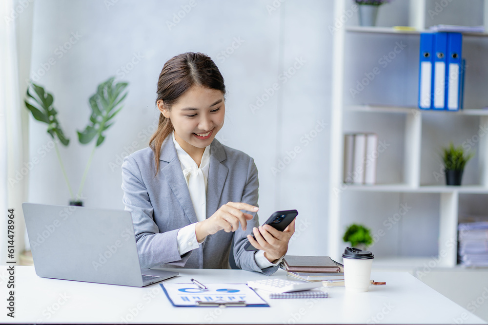 Smiling Asian woman talking on the phone with a customer Young positive female accountant using smartphone talking to team at her desk relaxing with mobile application Smiling Asian woman talking on the phone with a customer Young positive female accountant using smartphone talking to team at her desk relaxing with mobile application