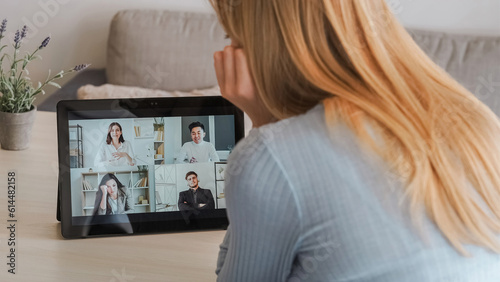 Home conference. Video office. Team tiredness. Online work challenges. Busy day. Back of woman sitting at table with tablet on call with exhausted colleagues.