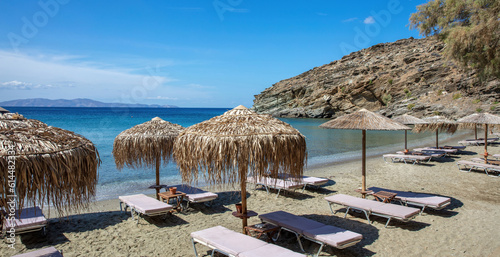 Fototapeta Naklejka Na Ścianę i Meble -  Straw umbrella, lounger in row on sandy empty beach summer sunny day. Tinos island Cyclades Greece.