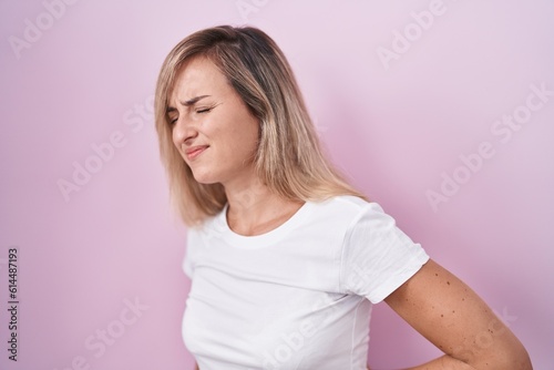 Young blonde woman standing over pink background suffering of backache  touching back with hand  muscular pain