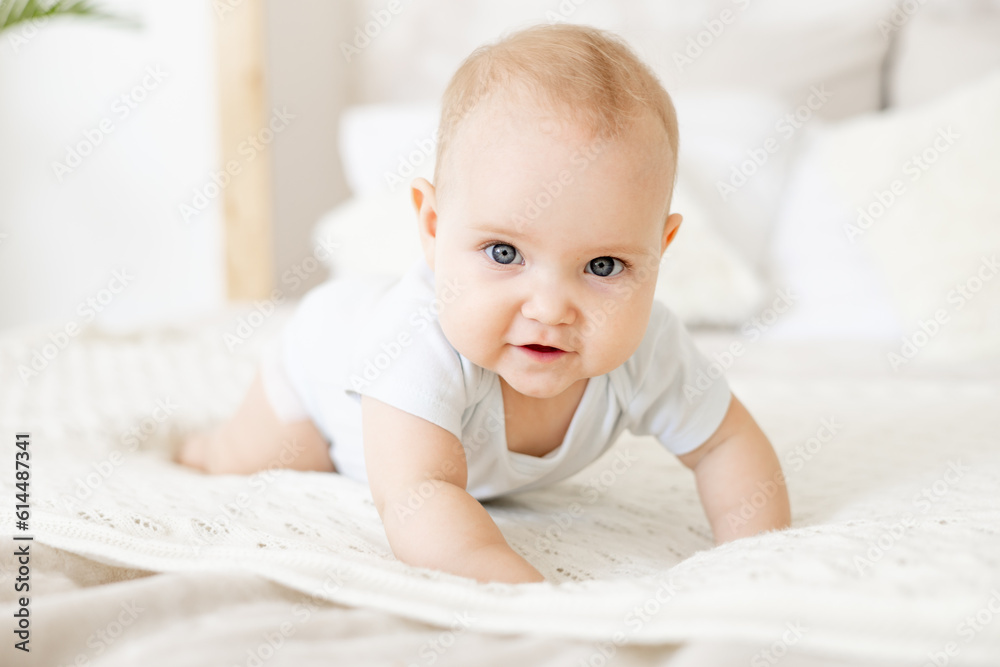 close-up of a happy baby on a white cotton bed in a bright bedroom, a small smiling baby boy or girl crawling