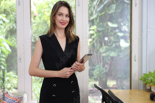 Modern beautiful businesswoman holding dogital taplet while standing in the office with green nature background photo