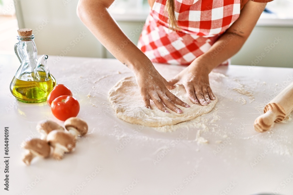 Young beautiful hispanic woman kneading dough pizza with hands at the kitchen