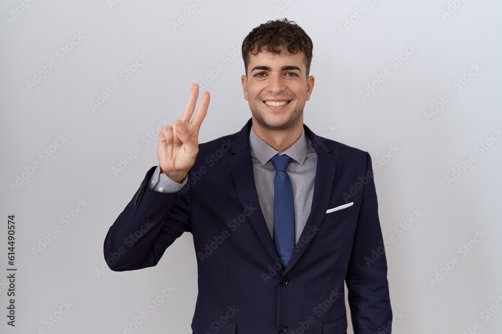 Young hispanic business man wearing suit and tie showing and pointing up with fingers number two while smiling confident and happy. Young hispanic business man wearing suit and tie showing and pointing up with fingers number two while smiling confident and happy.