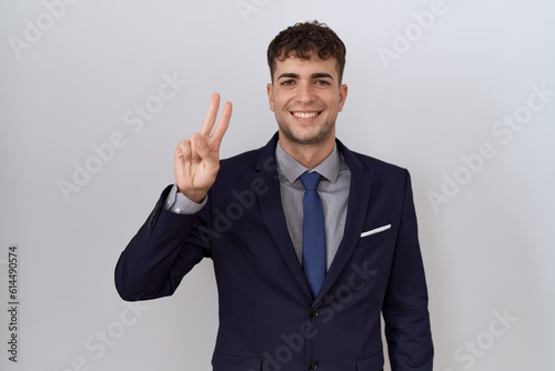 Young hispanic business man wearing suit and tie showing and pointing up with fingers number two while smiling confident and happy.