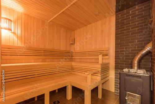 The interior of a traditional Finnish sauna made of light wood. Heating element at the brick wall.
