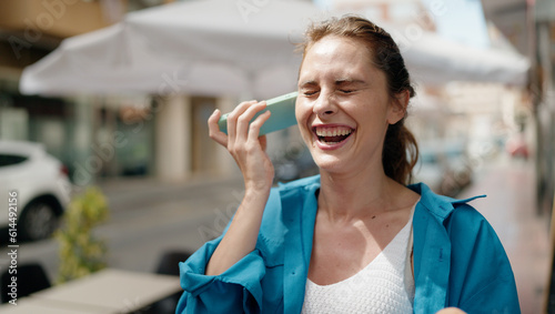 Young woman smiling confident listening audio message by the smartphone at street