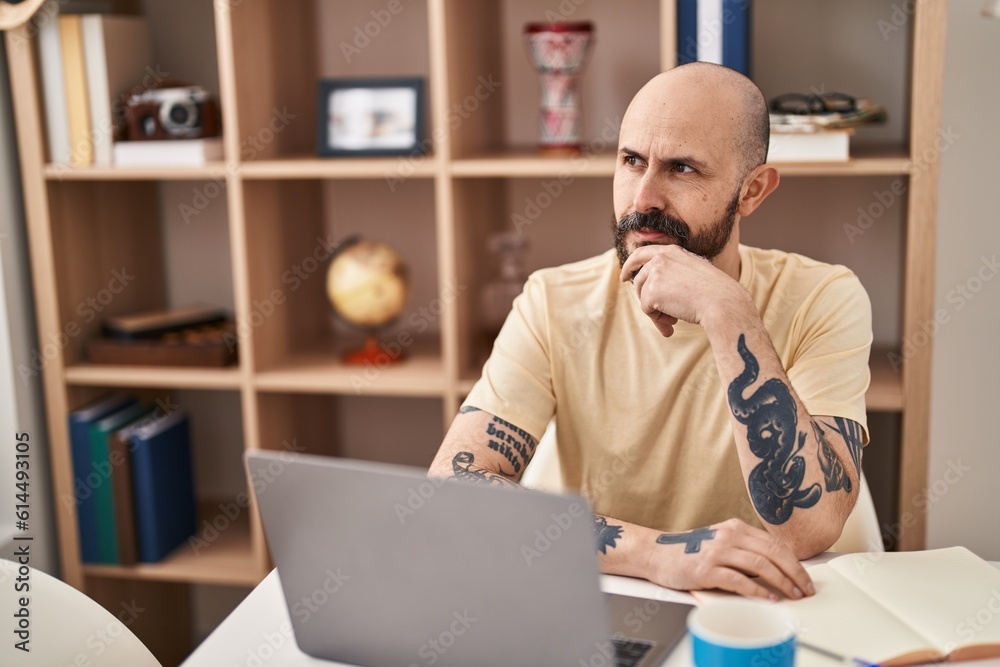 Young bald man using laptop sitting on table at home Young bald man using laptop sitting on table at home