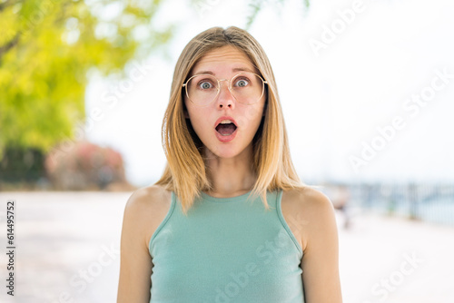 Young blonde woman at outdoors With glasses and surprised expression