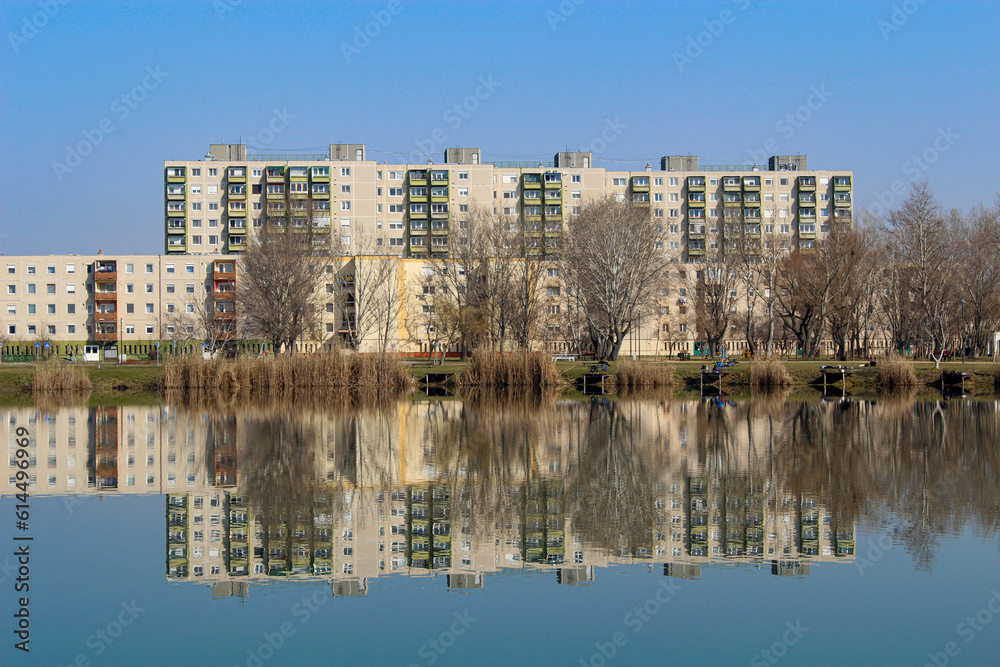 Colorful panel houses standing on the shore of a lake, reflected in the water. Housing estate in Hungary.