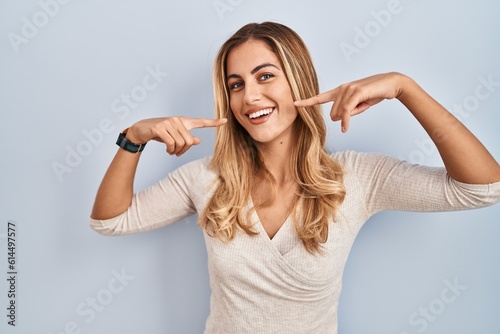 Fotografía Young blonde woman standing over isolated background smiling cheerful showing and pointing with fingers teeth and mouth