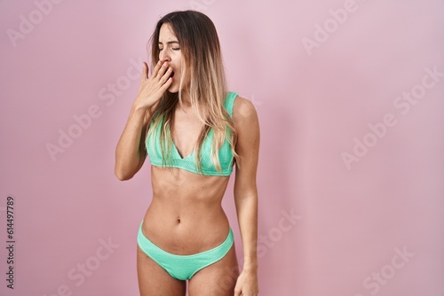 Young hispanic woman wearing bikini over pink background bored yawning tired covering mouth with hand. restless and sleepiness.