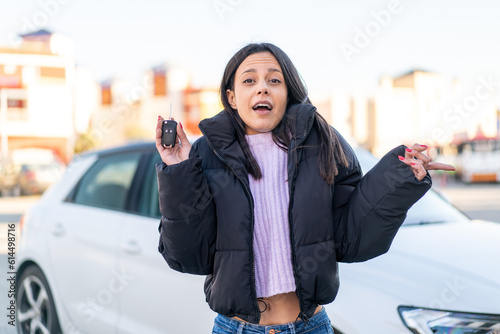 Young woman at outdoors holding car keys at outdoors surprised and pointing side