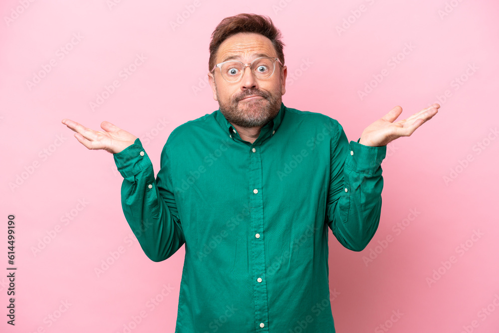 Middle age caucasian man isolated on pink background having doubts while raising hands Middle age caucasian man isolated on pink background having doubts while raising hands