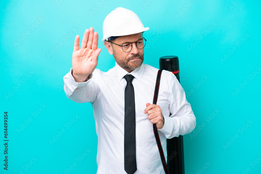Middle age architect man with helmet and holding blueprints isolated on blue background making stop gesture and disappointed Middle age architect man with helmet and holding blueprints isolated on blue background making stop gesture and disappointed