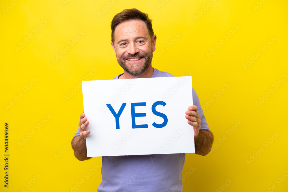 Middle age caucasian man isolated on yellow background holding a placard with text YES with happy expression Middle age caucasian man isolated on yellow background holding a placard with text YES with happy expression