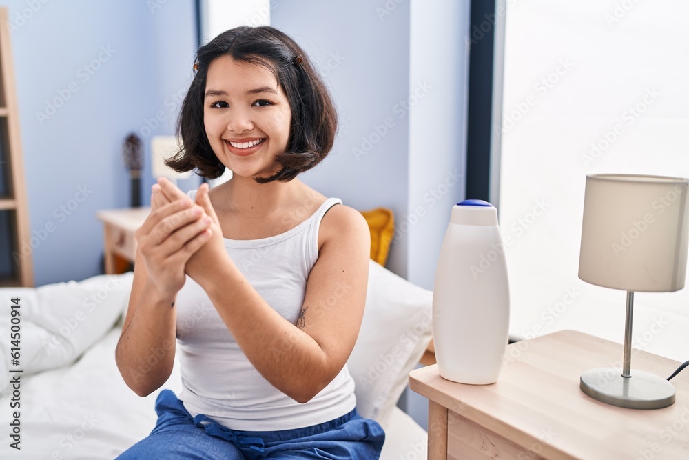 Young woman applying lotion on hands sitting on bed at bedroom Young woman applying lotion on hands sitting on bed at bedroom