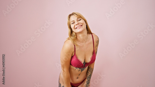 Young blonde woman wearing sensual lingerie standing smiling over isolated pink background