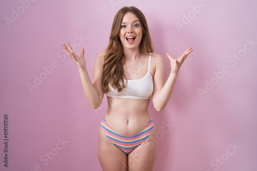 Caucasian woman wearing lingerie over pink background celebrating crazy and amazed for success with arms raised and open eyes screaming excited. winner concept © Krakenimages.com