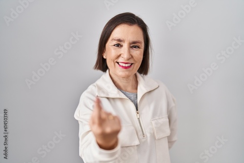 Middle age hispanic woman standing over isolated background beckoning come here gesture with hand inviting welcoming happy and smiling