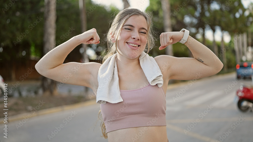 Young blonde woman wearing sportswear doing strong gesture with arms at street Young blonde woman wearing sportswear doing strong gesture with arms at street