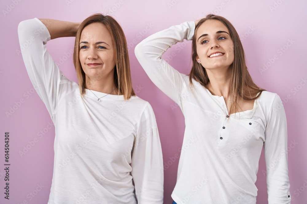 Middle age mother and young daughter standing over pink background smiling confident touching hair with hand up gesture, posing attractive and fashionable Middle age mother and young daughter standing over pink background smiling confident touching hair with hand up gesture, posing attractive and fashionable