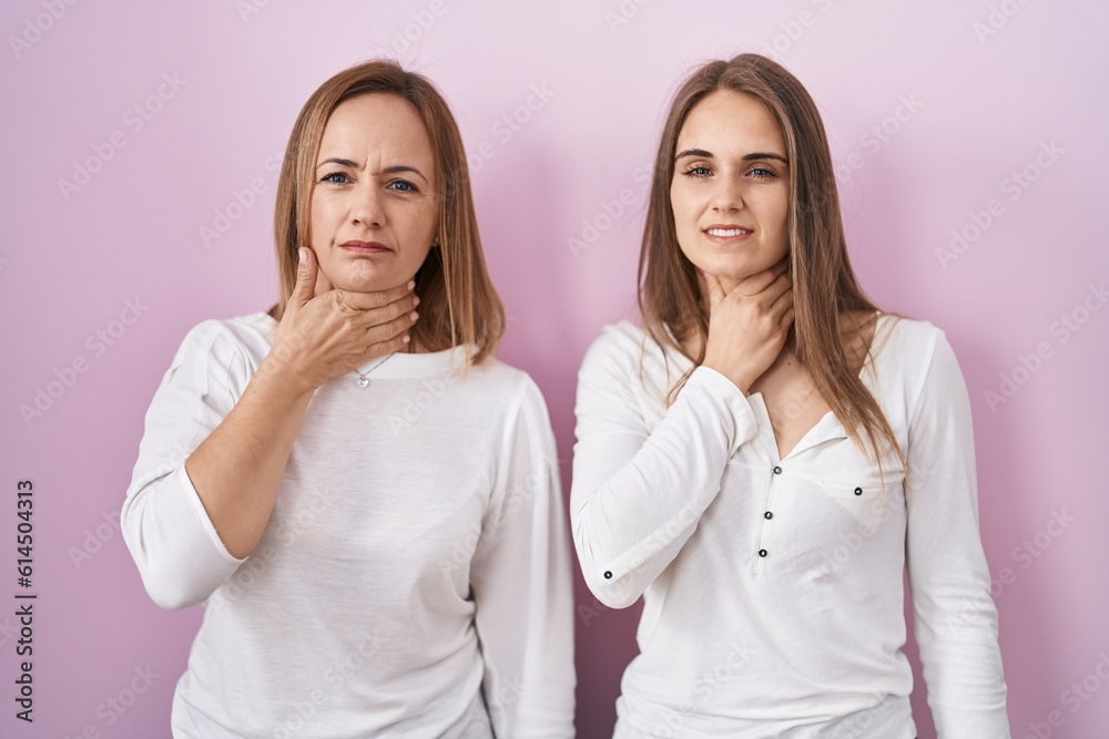 Middle age mother and young daughter standing over pink background touching painful neck, sore throat for flu, clod and infection Middle age mother and young daughter standing over pink background touching painful neck, sore throat for flu, clod and infection