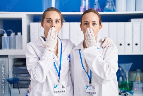 Two women working at scientist laboratory covering mouth with hand  shocked and afraid for mistake. surprised expression