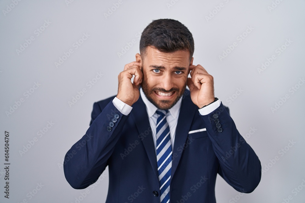 Handsome hispanic man wearing suit and tie covering ears with fingers with annoyed expression for the noise of loud music. deaf concept. Handsome hispanic man wearing suit and tie covering ears with fingers with annoyed expression for the noise of loud music. deaf concept.