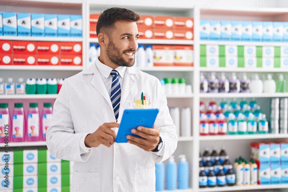 Young hispanic man pharmacist using touchpad working at pharmacy
