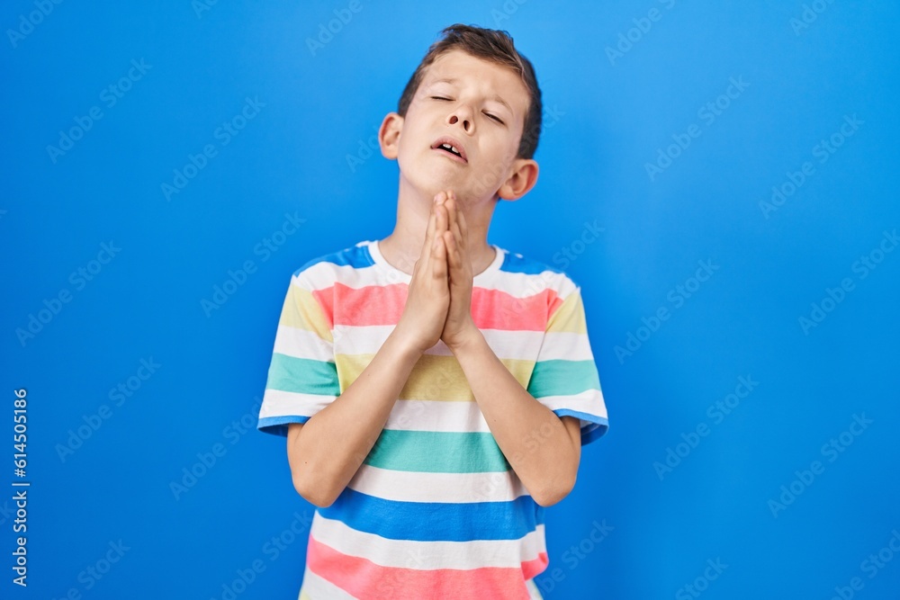 Young caucasian kid standing over blue background begging and praying with hands together with hope expression on face very emotional and worried. begging. Young caucasian kid standing over blue background begging and praying with hands together with hope expression on face very emotional and worried. begging.