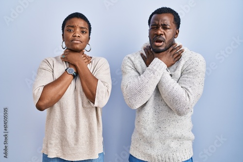 Young african american couple standing over blue background together shouting suffocate because painful strangle. health problem. asphyxiate and suicide concept.