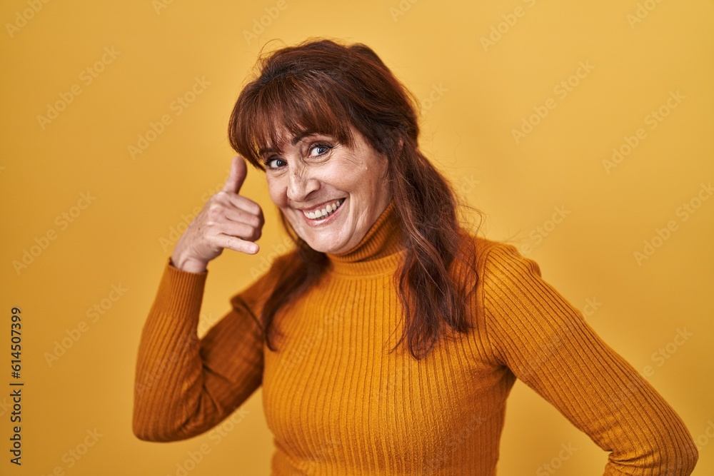 Middle age hispanic woman standing over yellow background smiling doing phone gesture with hand and fingers like talking on the telephone. communicating concepts. Middle age hispanic woman standing over yellow background smiling doing phone gesture with hand and fingers like talking on the telephone. communicating concepts.