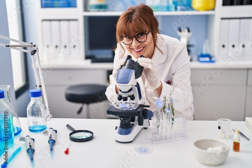 Middle age woman scientist smiling confident using microscope at laboratory