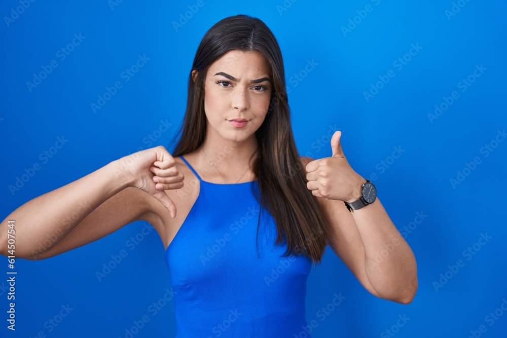 Hispanic woman standing over blue background doing thumbs up and down, disagreement and agreement expression. crazy conflict Hispanic woman standing over blue background doing thumbs up and down, disagreement and agreement expression. crazy conflict