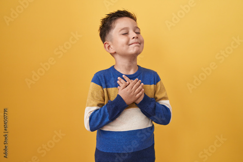 Little hispanic boy standing over yellow background smiling with hands on chest, eyes closed with grateful gesture on face. health concept. photo