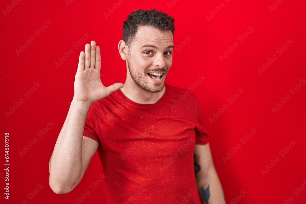 Young hispanic man standing over red background waiving saying hello happy and smiling, friendly welcome gesture Young hispanic man standing over red background waiving saying hello happy and smiling, friendly welcome gesture