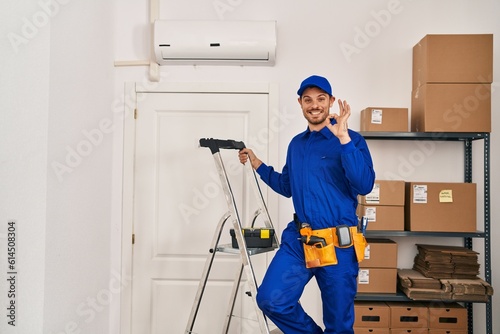 Young hispanic man working at renovation doing ok sign with fingers, smiling friendly gesturing excellent symbol