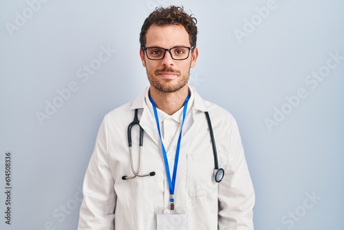 Young hispanic man wearing doctor uniform and stethoscope relaxed with serious expression on face. simple and natural looking at the camera.