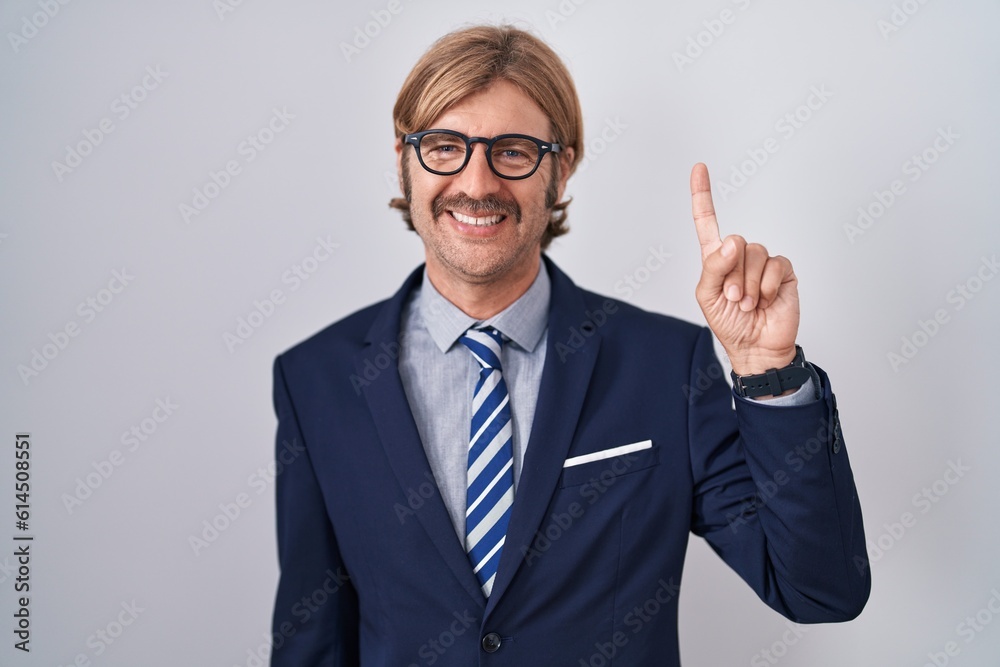 Caucasian man with mustache wearing business clothes showing and pointing up with finger number one while smiling confident and happy. Caucasian man with mustache wearing business clothes showing and pointing up with finger number one while smiling confident and happy.
