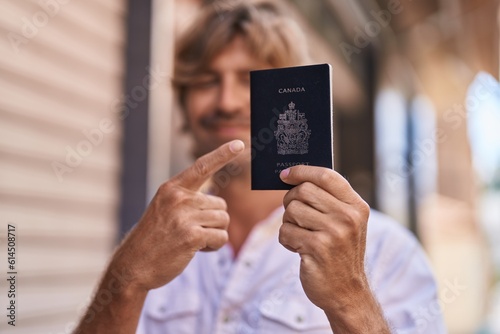 Young man smiling confident pointing with finger to passport at street photo